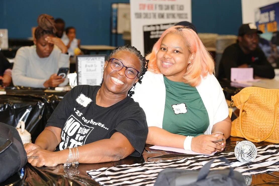 Two smiling women sitting at a table with black and white striped cloth.