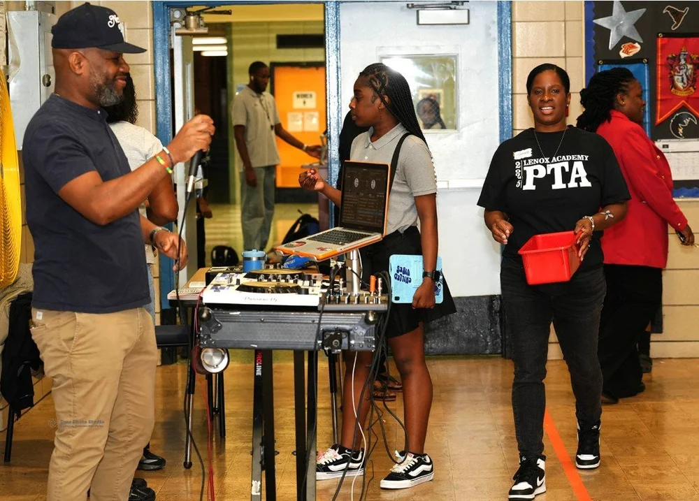 Man holding a microphone near a DJ setup with a young woman operating a laptop.