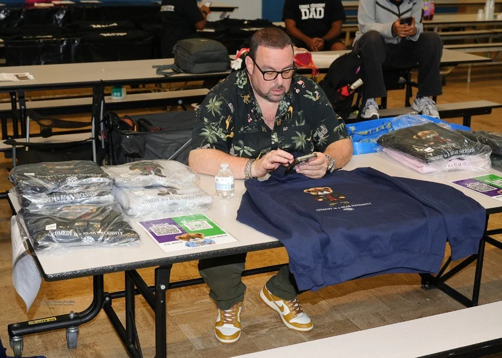 Man with glasses sitting at a table displaying packaged sweatshirts