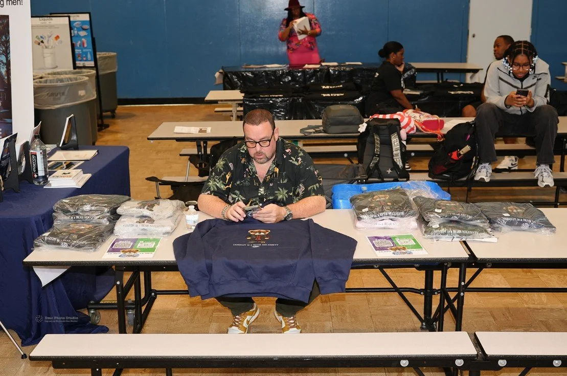 A man sitting behind a table displaying folded sweatshirts 