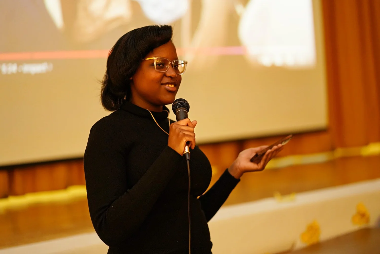 Woman in glasses speaking into a microphone while holding a phone