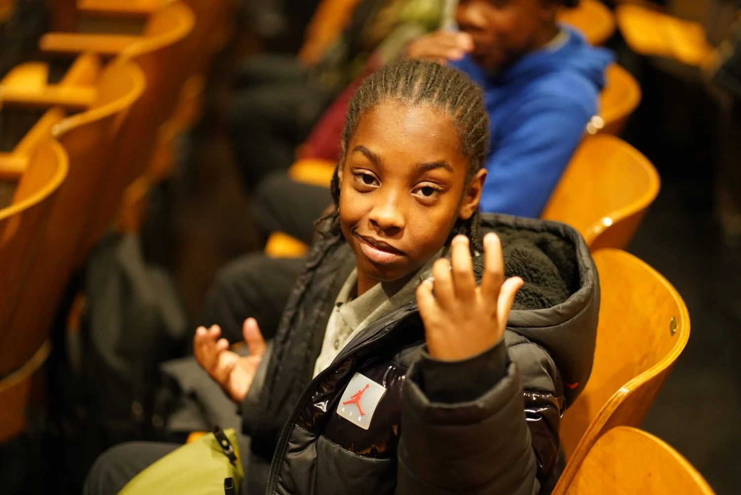 Smiling young person with braided hair in a black jacket seated
