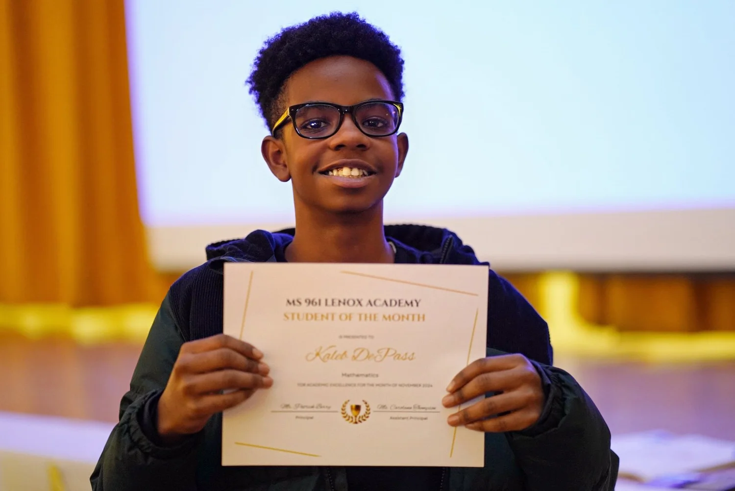 Smiling teenage boy wearing glasses holding a 'Student of the Month' certificate.