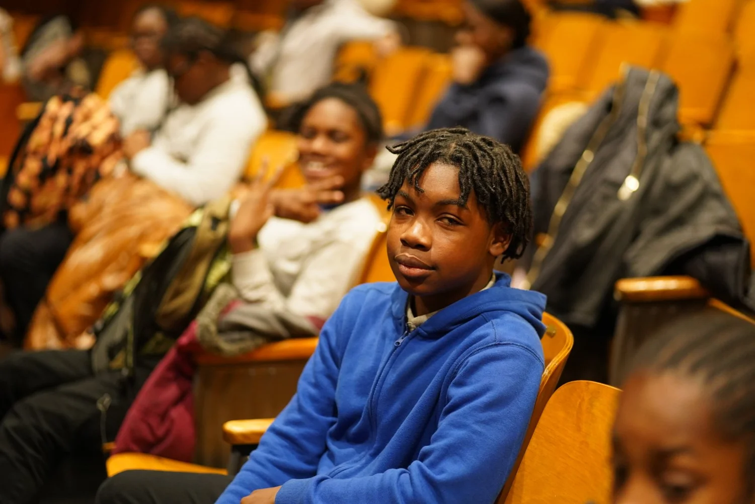 Teenager in a blue hoodie sitting in an auditorium 