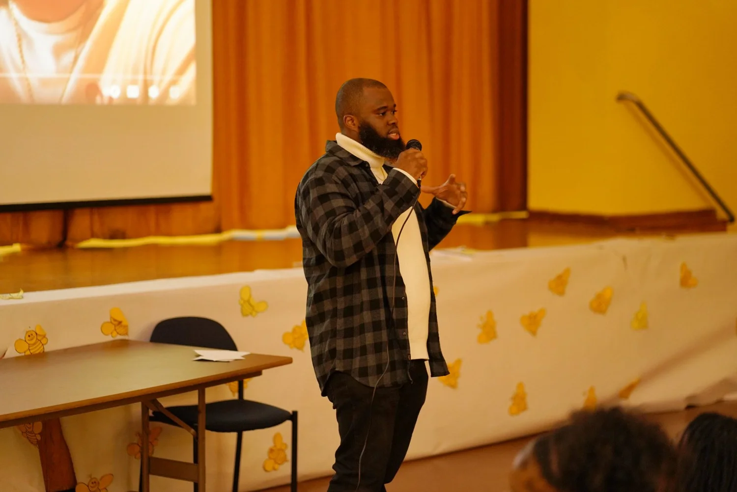 A bearded man in a black and gray checkered shirt speaking
