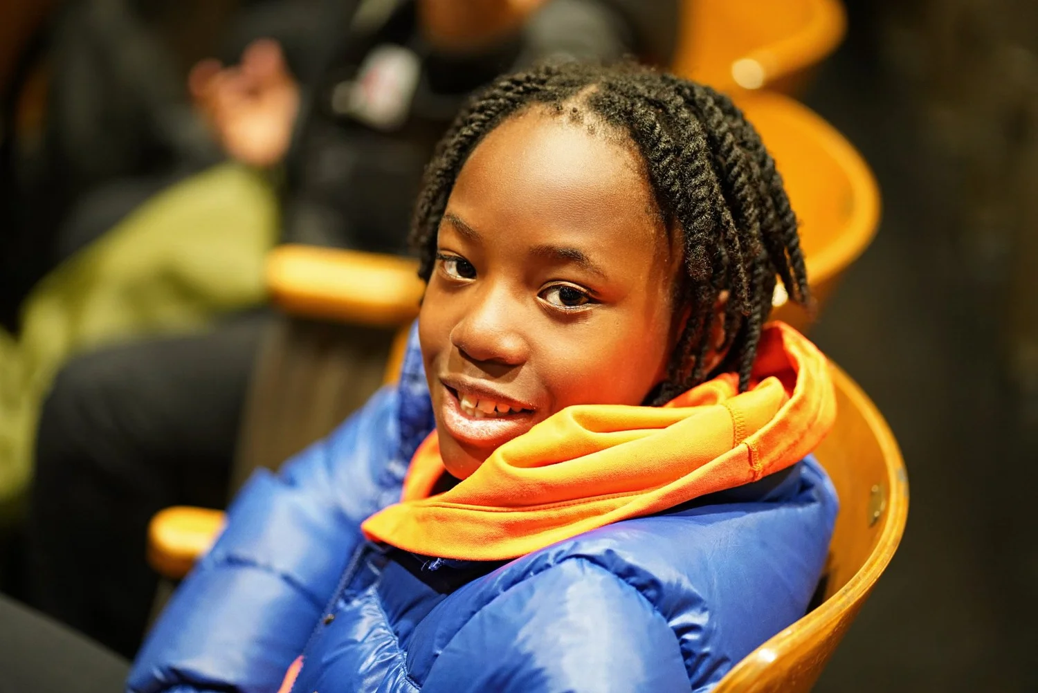Smiling young person with braided hair wearing a blue jacket 