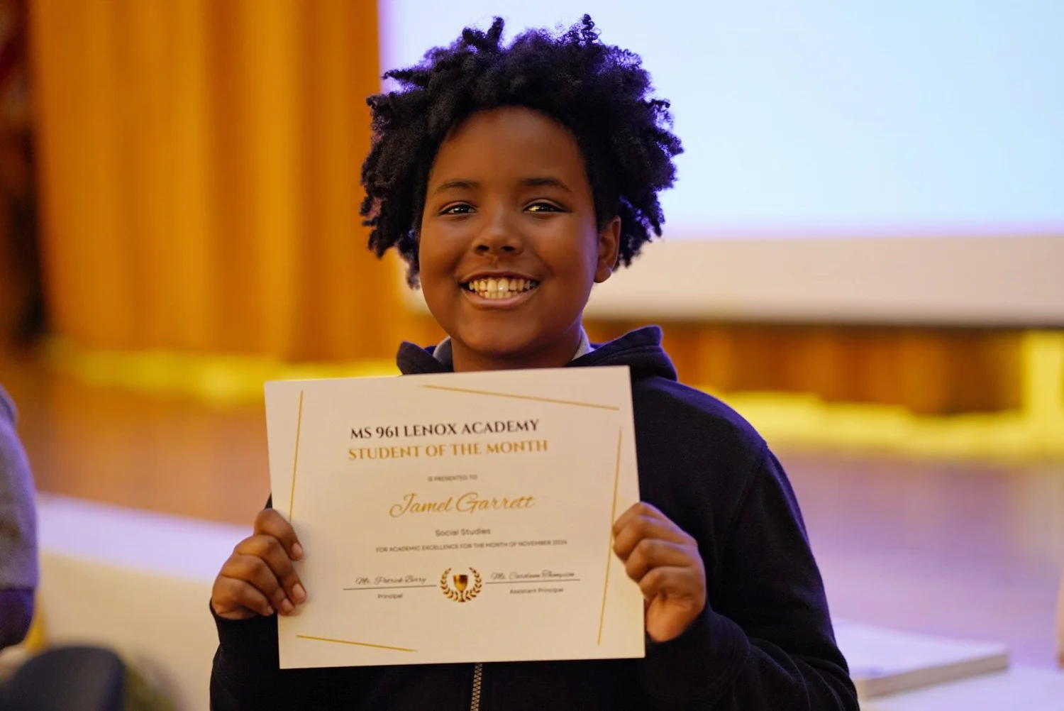 Smiling student holding a certificate for Student of the Month at MS 961 Lenox Academy.