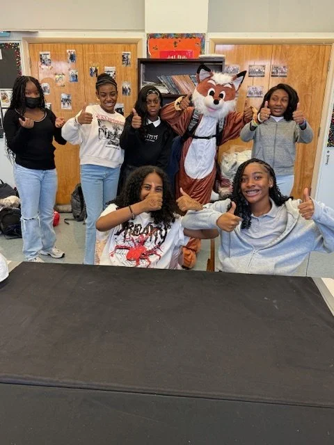 Group of seven smiling teenagers posing indoors with a person in a fox mascot costume