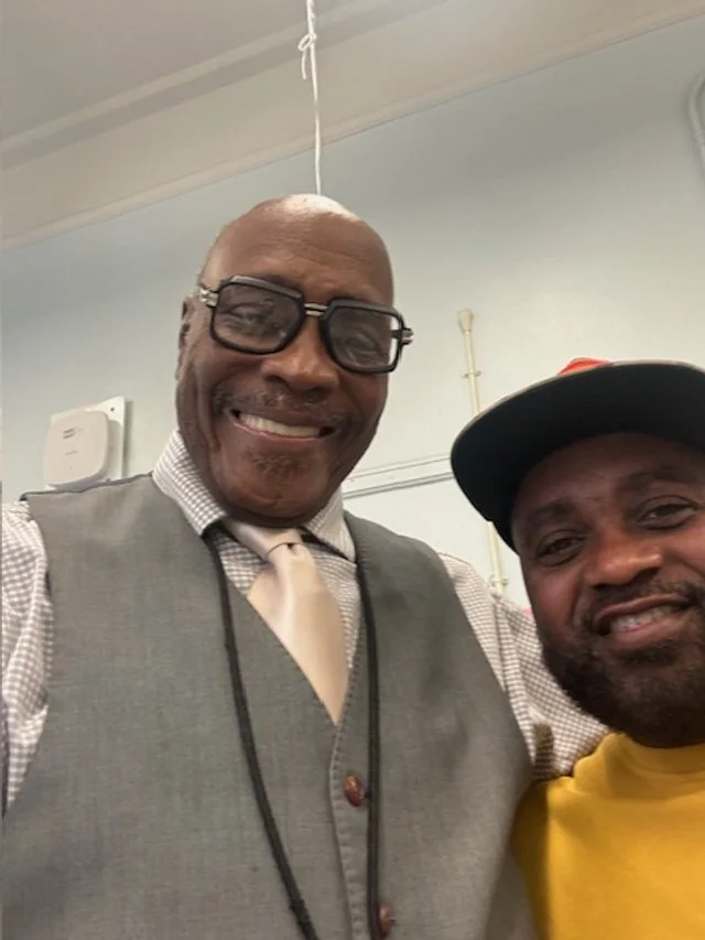 Two smiling men posing for a selfie indoors, one wearing glasses