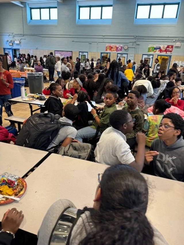 A crowded school cafeteria with students sitting and standing