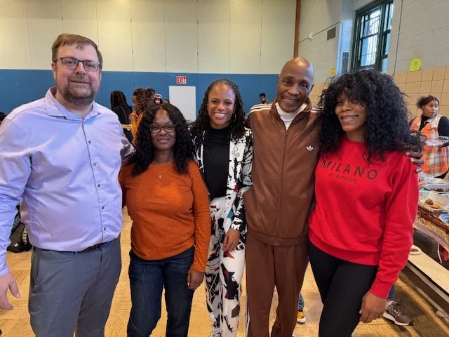 Five adults smiling and posing together in a gymnasium