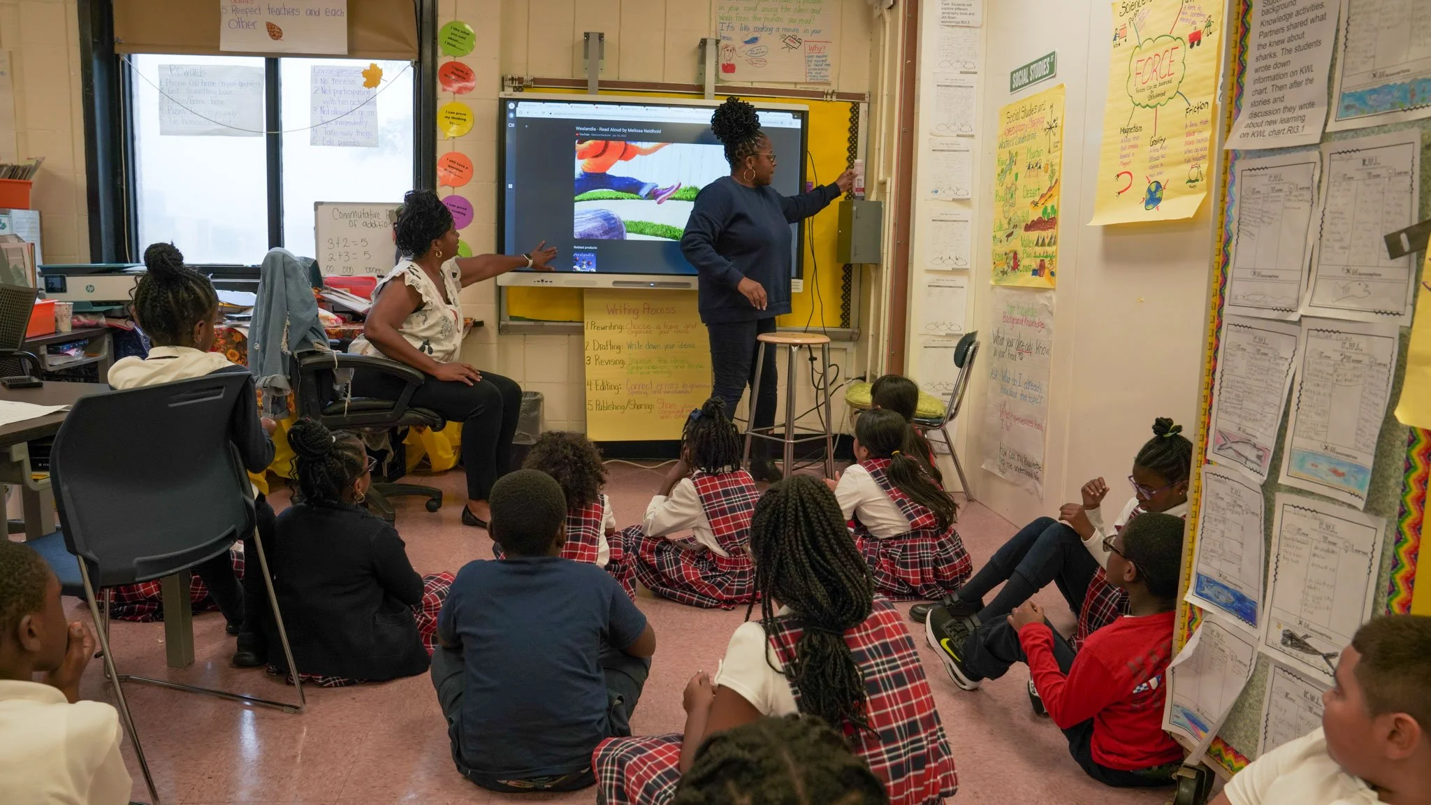 Woman in a bright pink dress with pearl necklace and breast cancer awareness ribbon pin, standing confidently indoors.