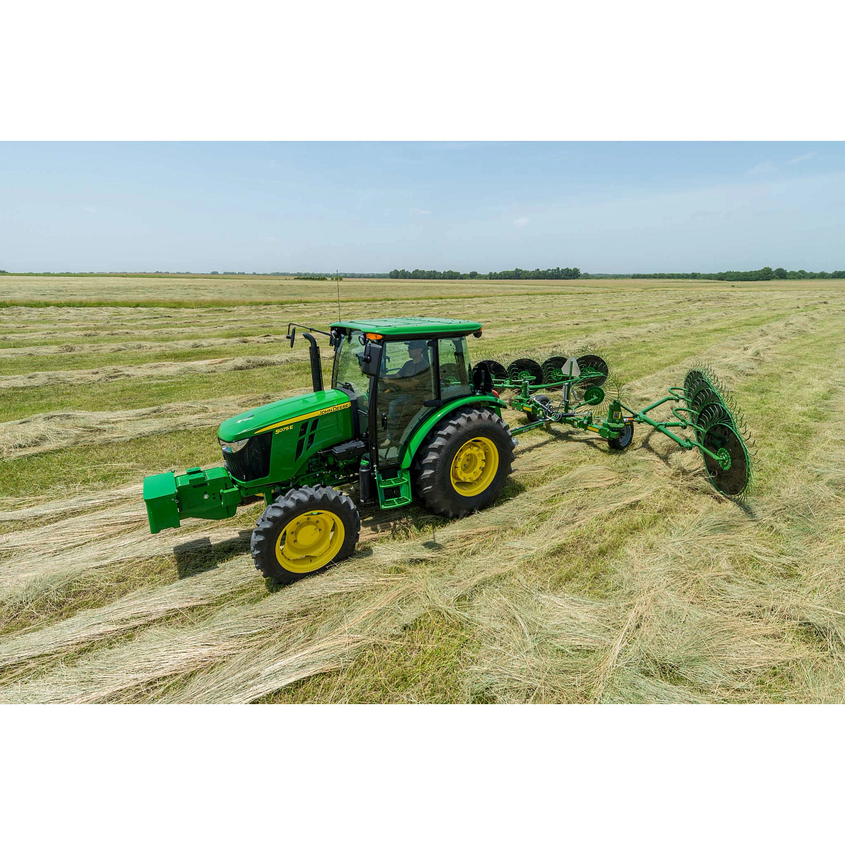 Side left view of a 5075E tractor with attached WR00 series wheel rake at work in a hay field