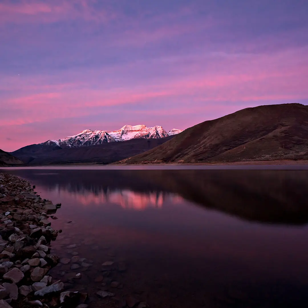 Stunning view of snow-capped Mount Timpanogos reflecting in a calm lake at sunset, showcasing natural beauty near Midway, Utah.