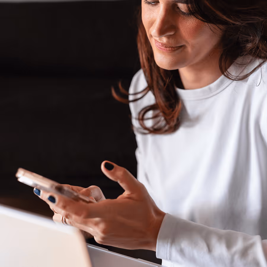 Woman wearing a white long-sleeve shirt looking down at her smartphone with a slight smile.