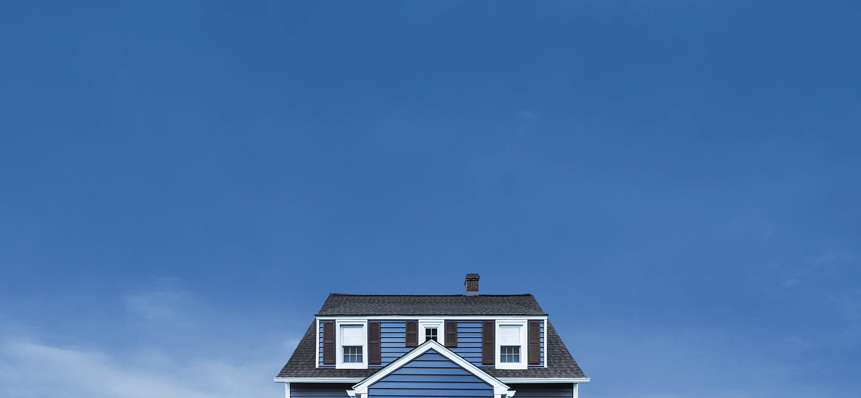 Blue house roof with two dormer windows and a chimney under a clear blue sky.