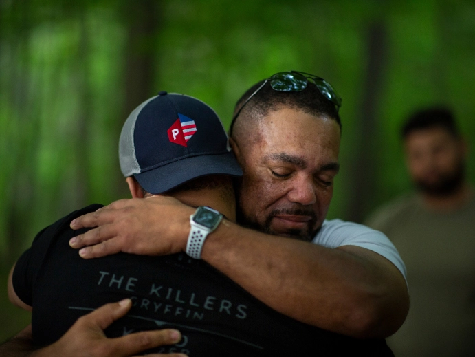 Two men embracing each other warmly in an outdoor forest setting.