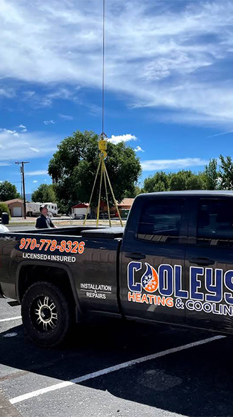 Black Cooleys Heating & Cooling truck parked outdoors under a partly cloudy sky.