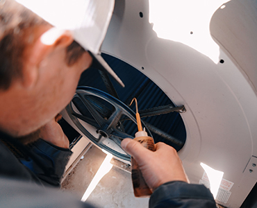 Technician lubricating the belt and pulley system inside an HVAC unit.