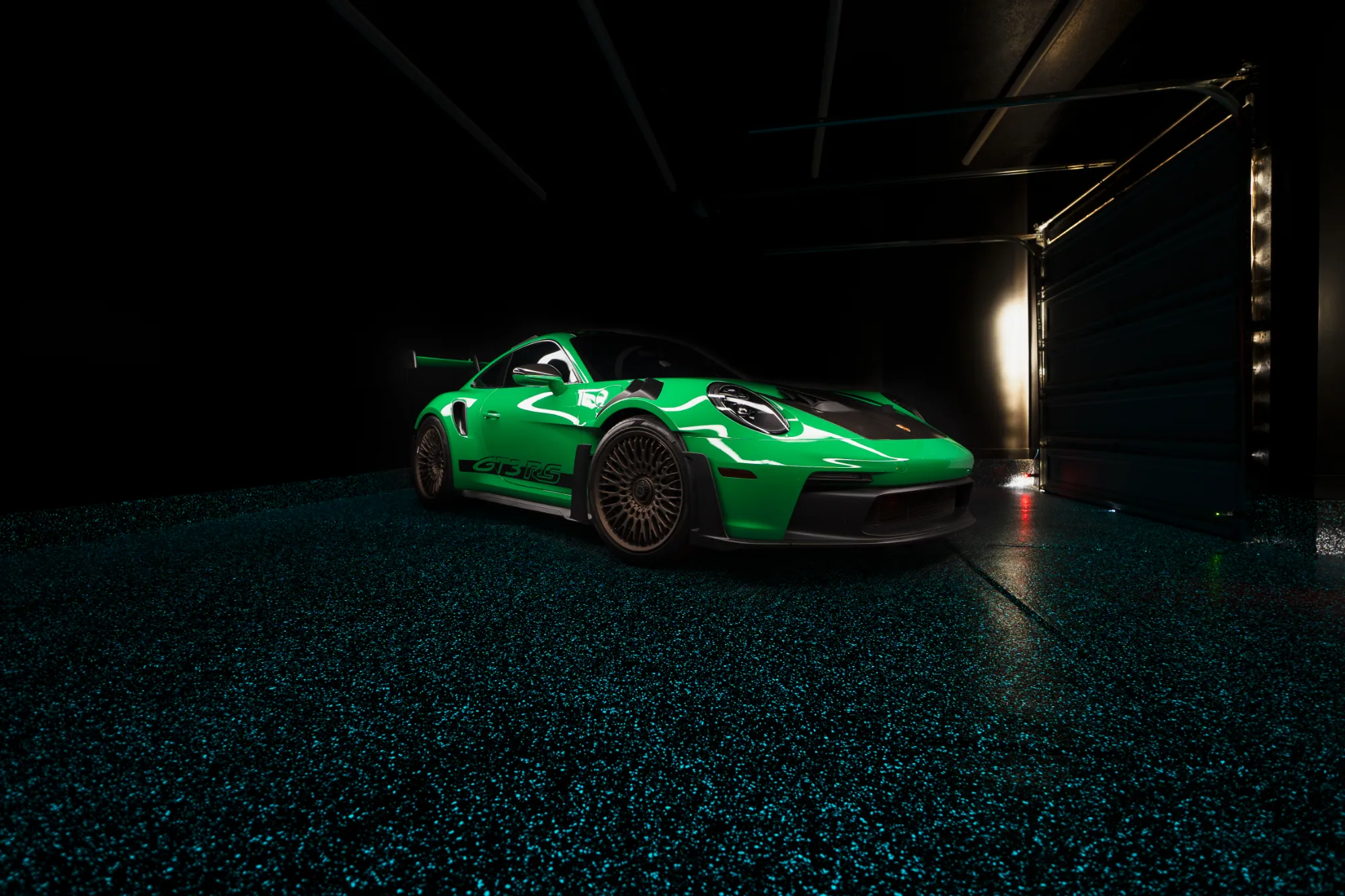 Bright green Porsche GT3 RS sports car parked on a dark garage floor with blue glow-in-the-dark speckles.