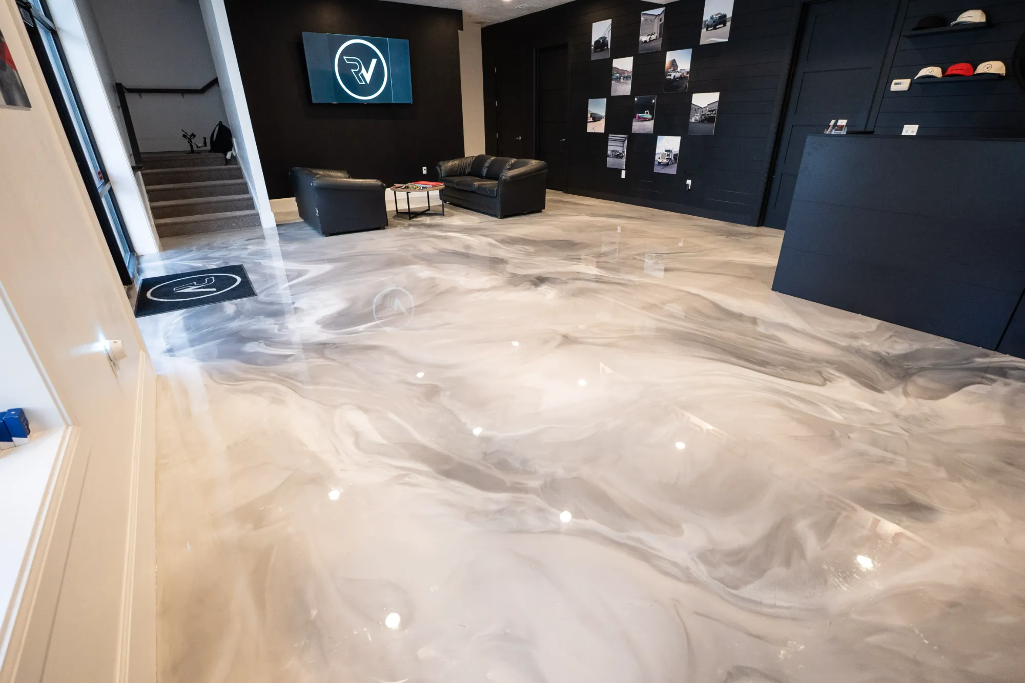 Modern office lobby with glossy, marbled epoxy floor, black leather sofas, black walls, and a TV screen displaying a circular RV logo.