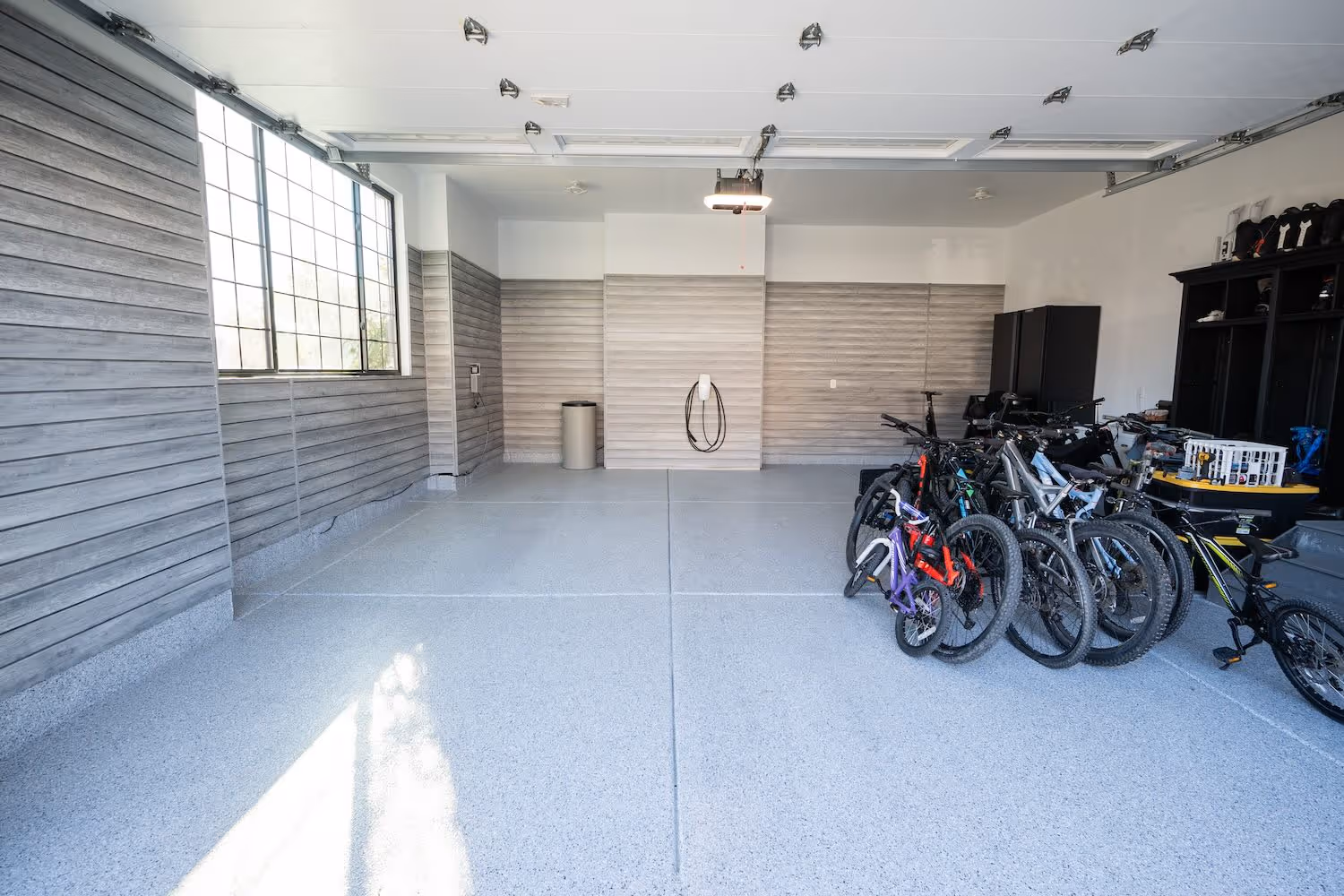 Modern garage with gray textured walls, a row of bicycles on the right, and an EV charging station mounted on the back wall.