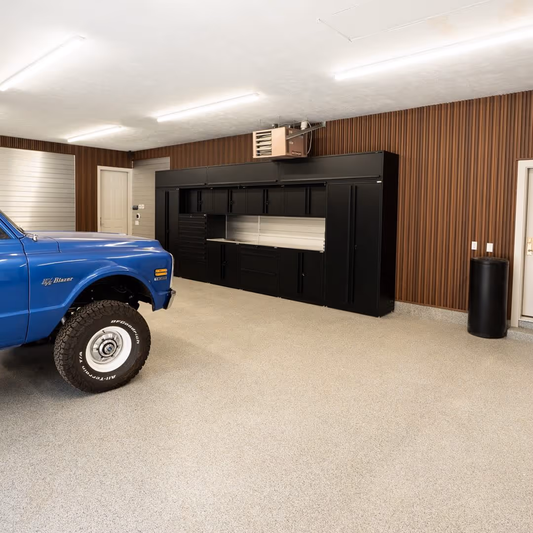 Clean garage interior with a blue vintage K5 Blazer truck front and black storage cabinets against a wood-paneled wall.