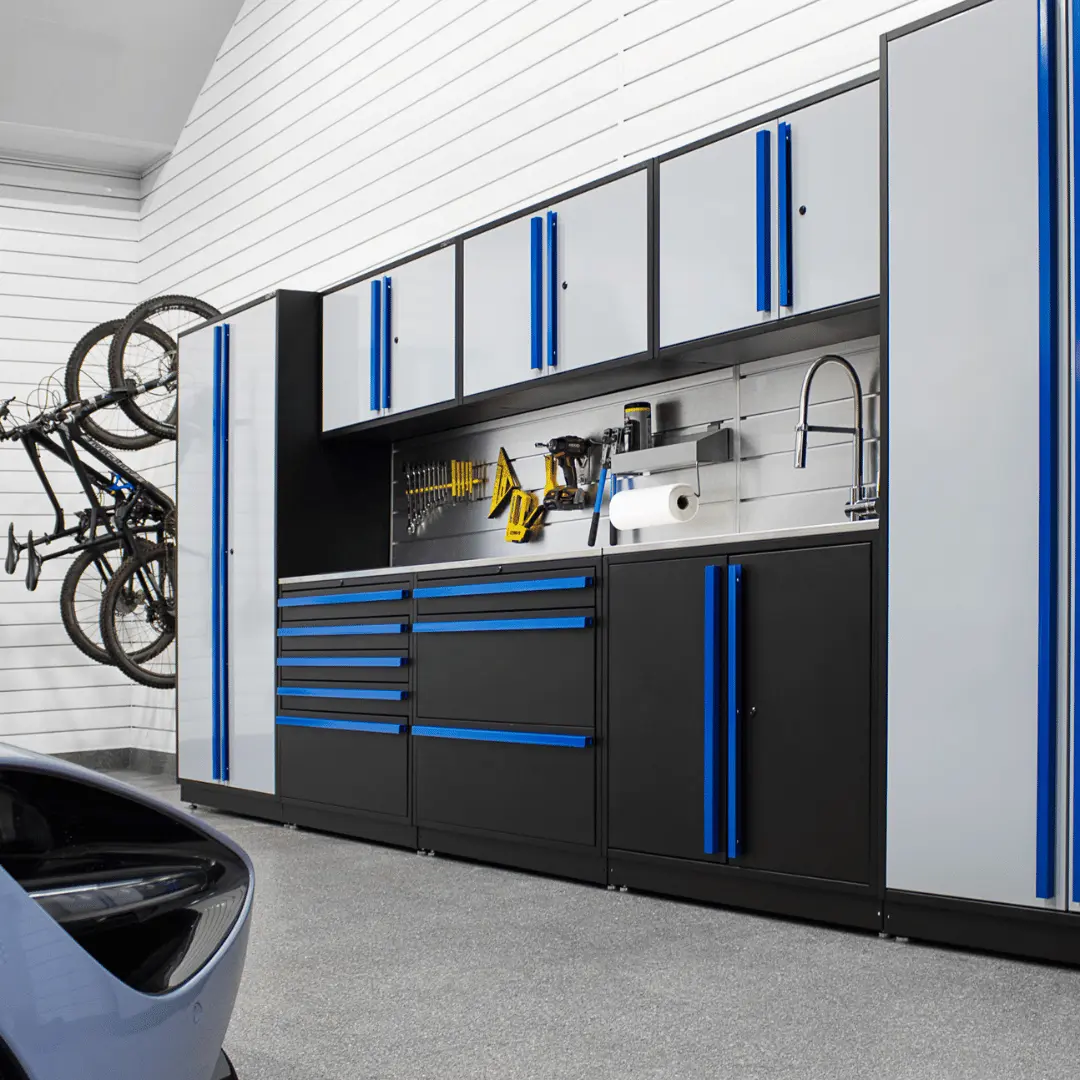 Modern garage interior with gray and black cabinets featuring blue handles, a wall-mounted bike rack with two bicycles, tools organized on the wall, and a partial view of a vehicle.