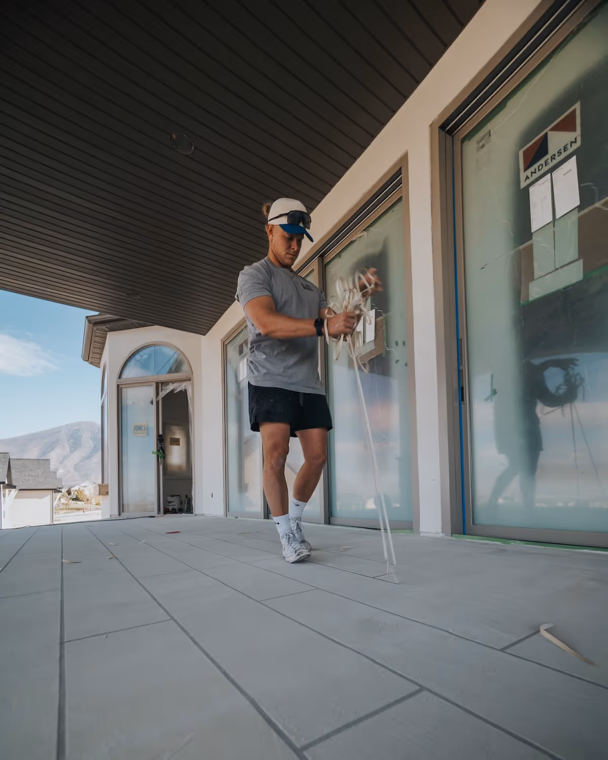 Man in casual clothing standing on a tiled porch while holding a bundle of white rope or cables in his hands.
