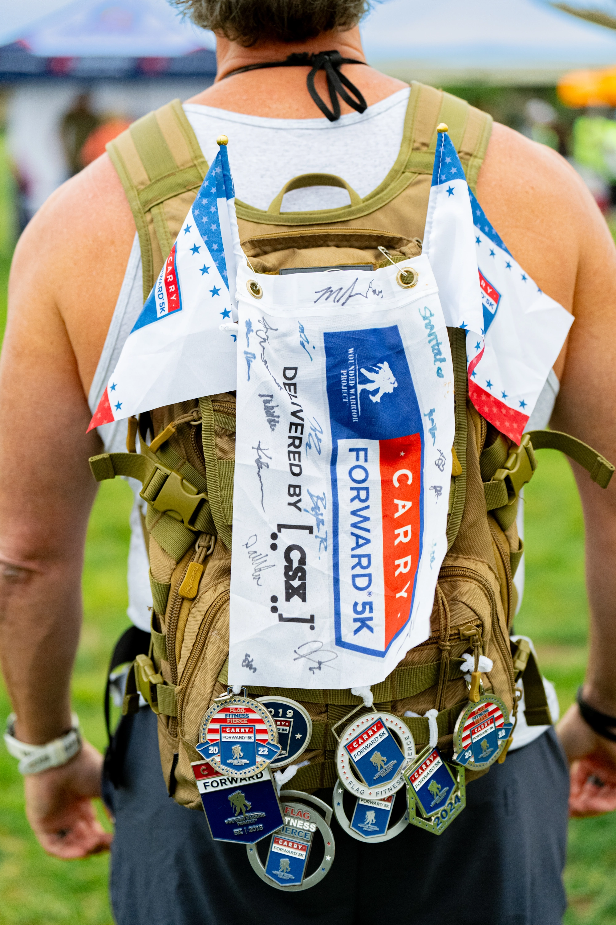 Person wearing a backpack with signed Carry Forward 5K flag and multiple medals attached.