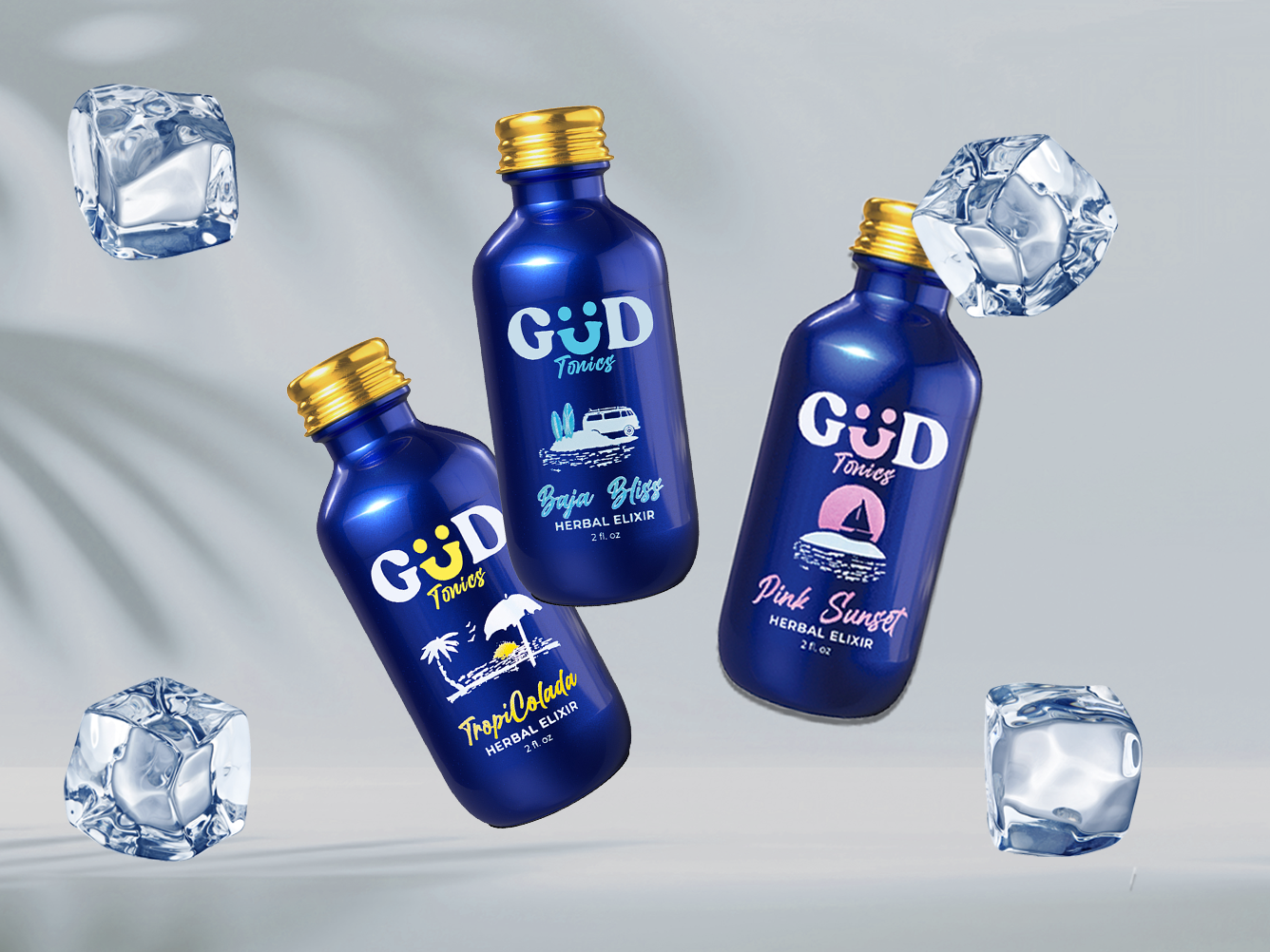 Three blue bottles of GÜD Tonics herbal elixirs labeled TropiColada, Baja Bliss, and Pink Sunset surrounded by floating ice cubes.
