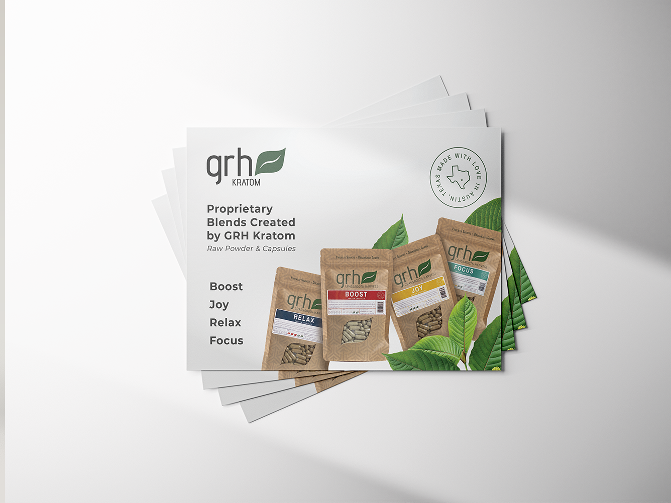 Stack of postcards showing GRH Kratom packaging with four blends: Boost, Joy, Relax, and Focus in capsules and powder form alongside green leaves and a Texas-made stamp.