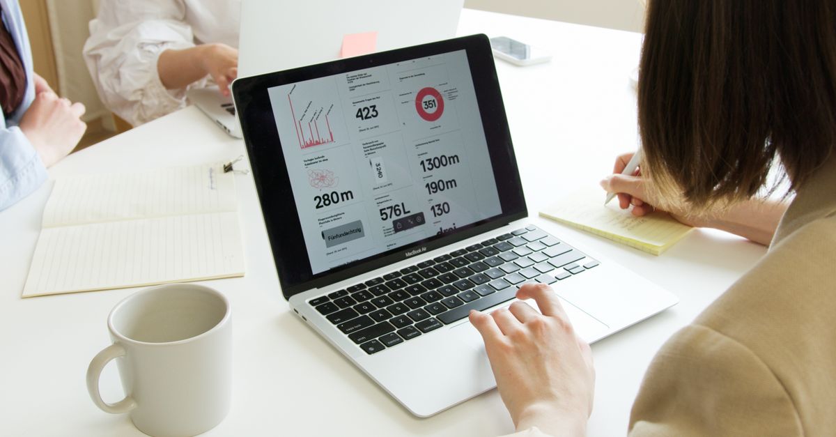 Laptop mit einer Auswertung auf dem Bildschirm, daneben schreibt eine Person mit