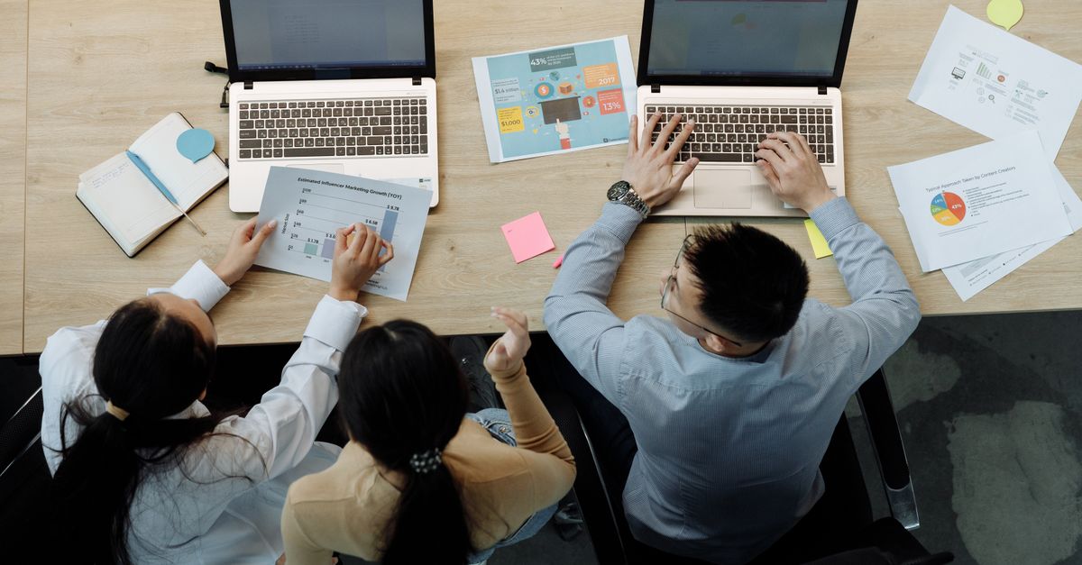 Vier Personen arbeiten von oben gesehen mit Laptops an einem Tisch