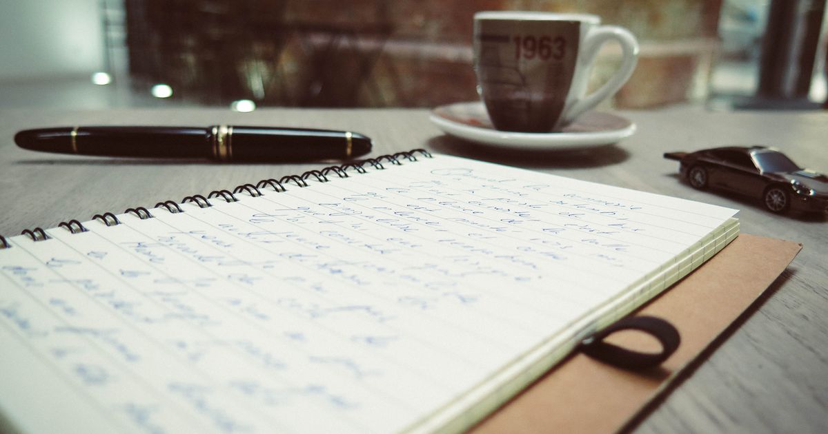 Person schreibt Anforderungen in ein Notizbuch am Schreibtisch