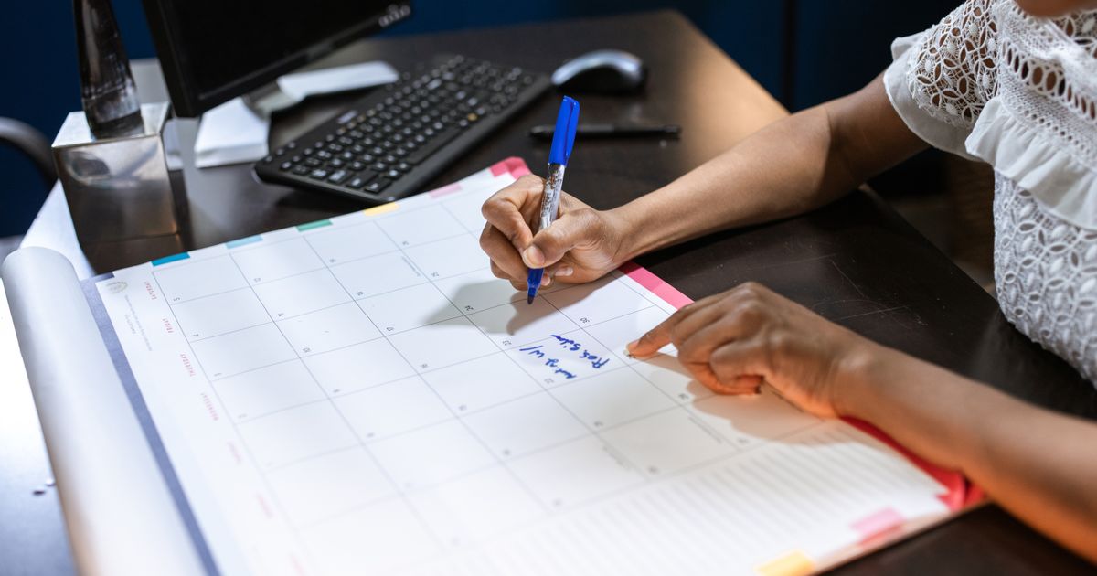 Person trägt mit einem Stift Notizen in einen Tischkalender ein