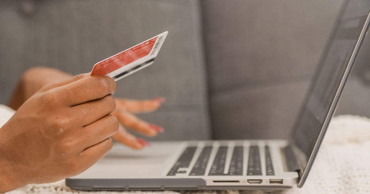Person hält eine Kreditkarte vor einen Laptop