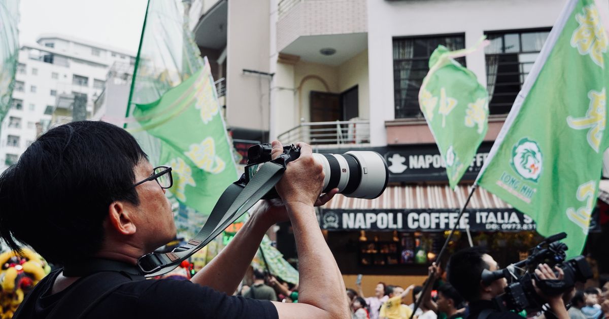 Fotograf mit Teleobjektiv fotografiert einen Umzug mit Fahnen
