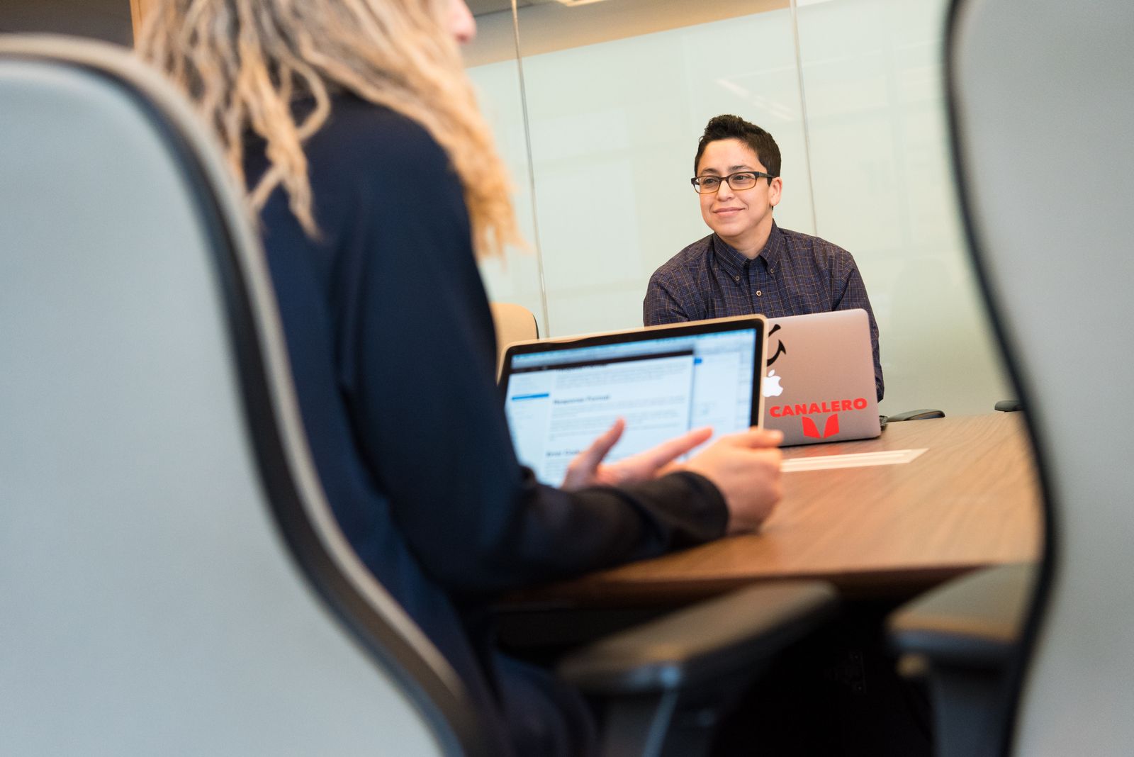 Zwei Personen im Gespräch an einem Besprechungstisch mit Laptops