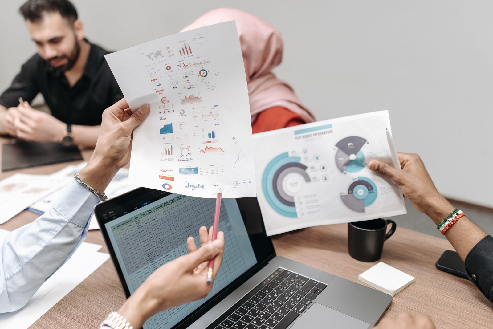 Mehrere Hände zeigen auf Diagramme auf Papier neben einem Laptop