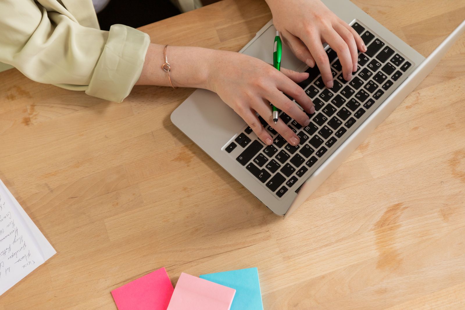 Hände tippen auf einem Laptop, daneben Stift und bunte Notizzettel