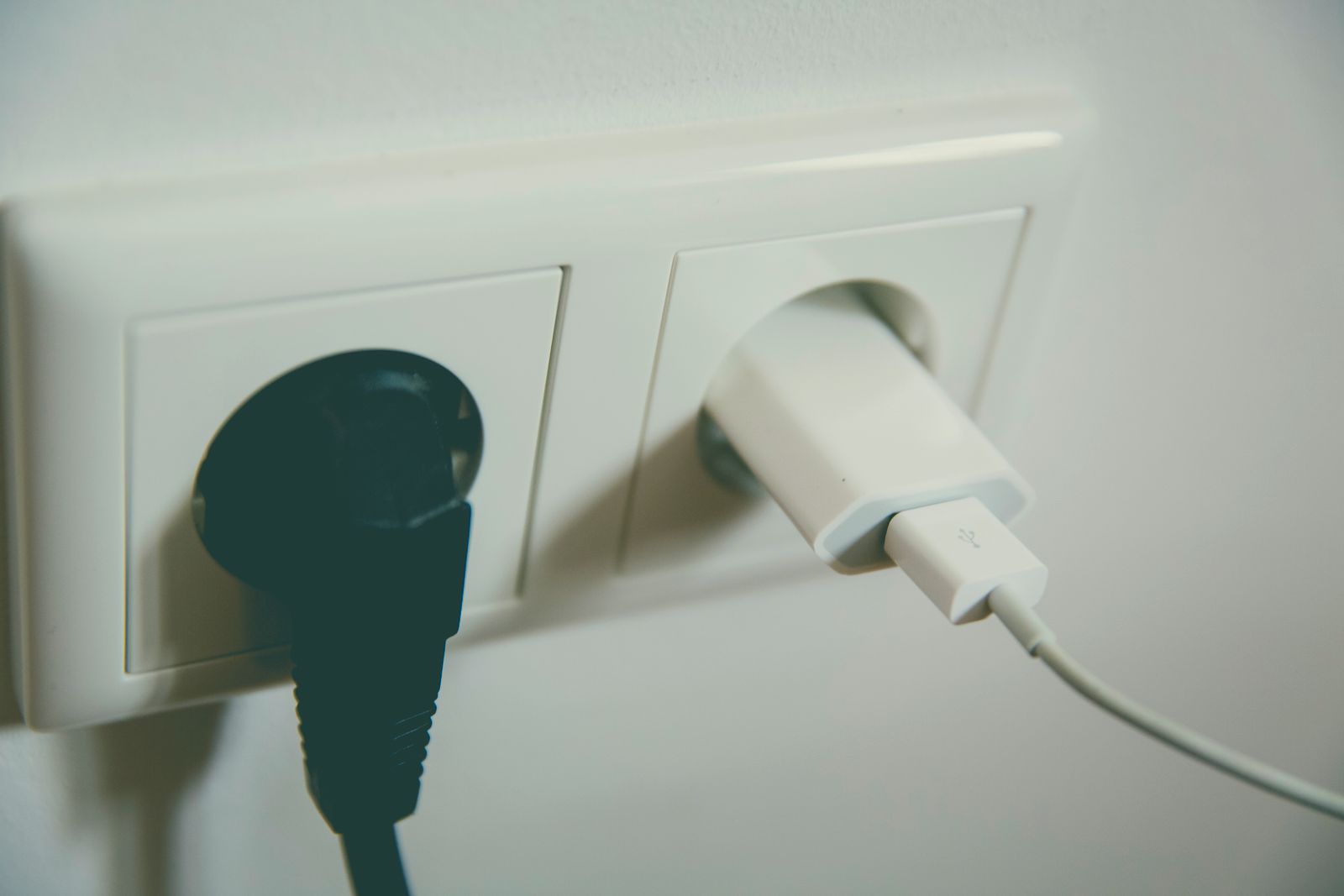 Zwei Stecker in einer Doppelsteckdose an einer hellen Wand