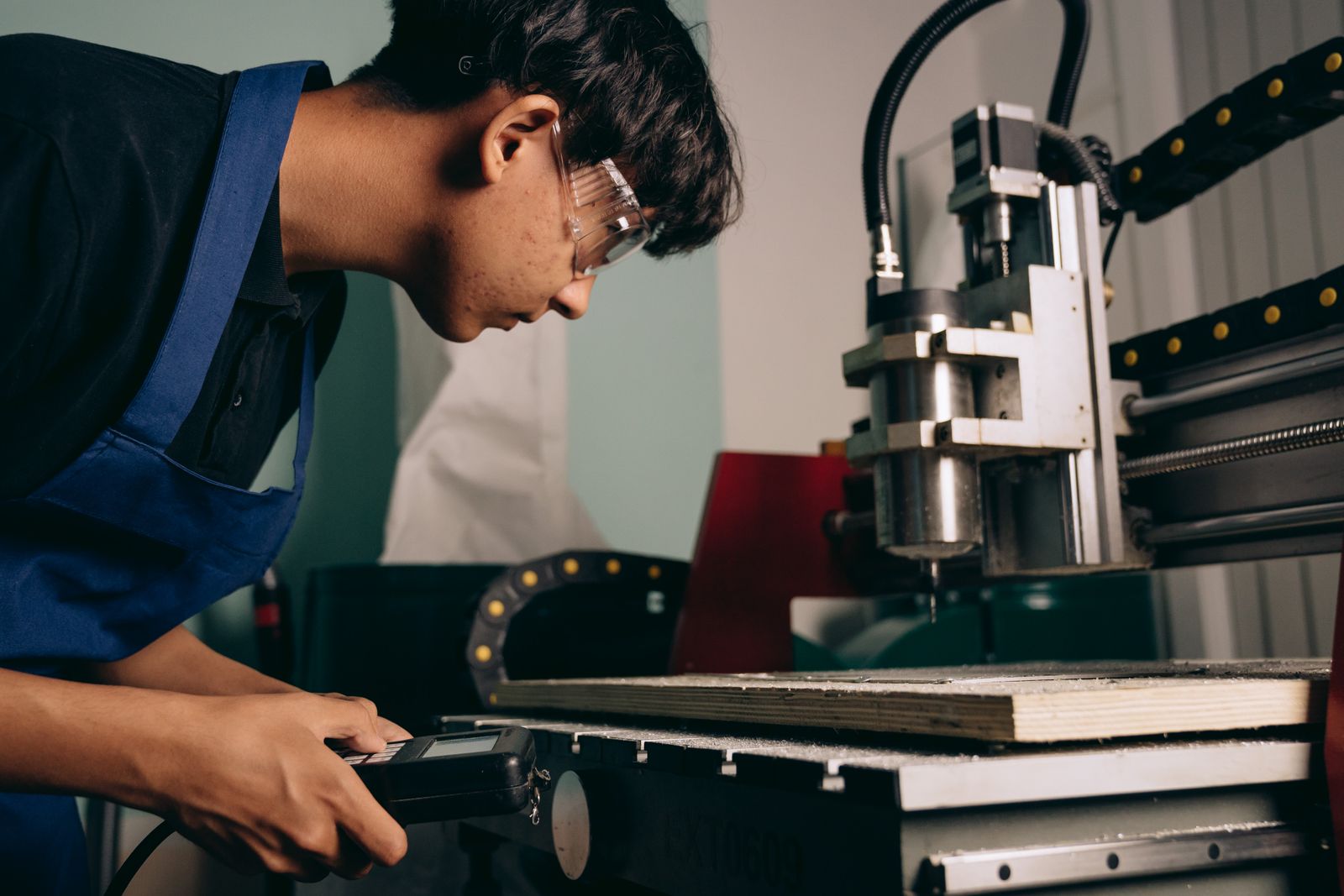 Junger Mann mit Schutzbrille arbeitet in einer Werkstatt an einer Maschine