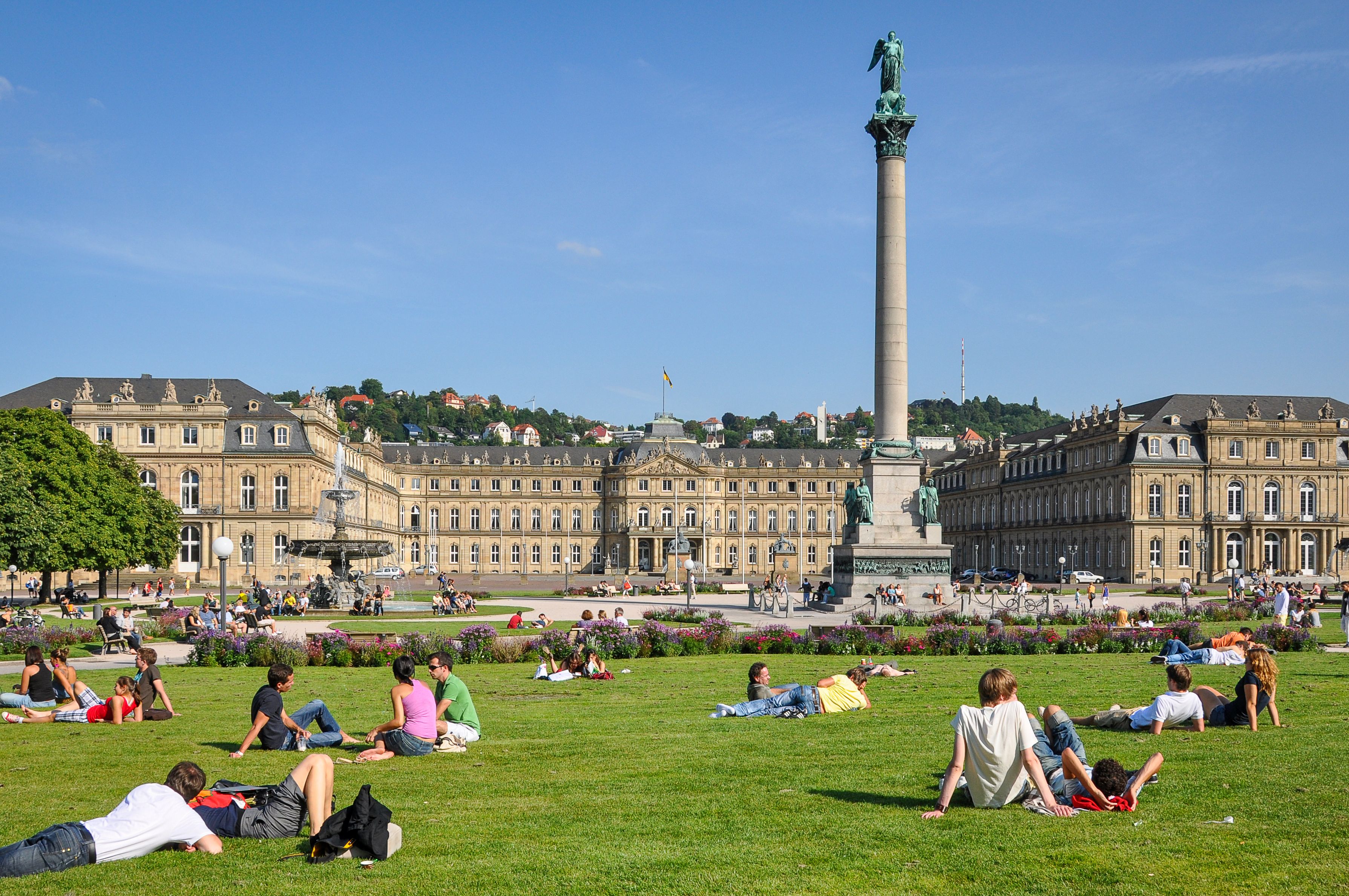Schlossplatz in Stuttgart mit dem Neuen Schloss und Menschen auf der Wiese bei Sonnenschein