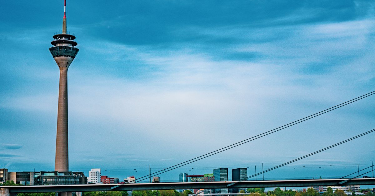 Rheinturm in Düsseldorf mit Rheinkniebrücke und einem Schiff auf dem Rhein unter bewölktem Himmel