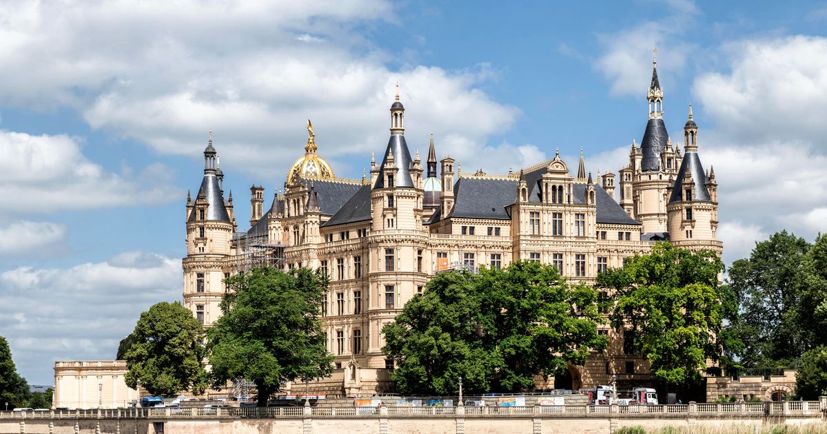 Schweriner Schloss mit Türmen und Kuppeln hinter Bäumen unter blauem Himmel