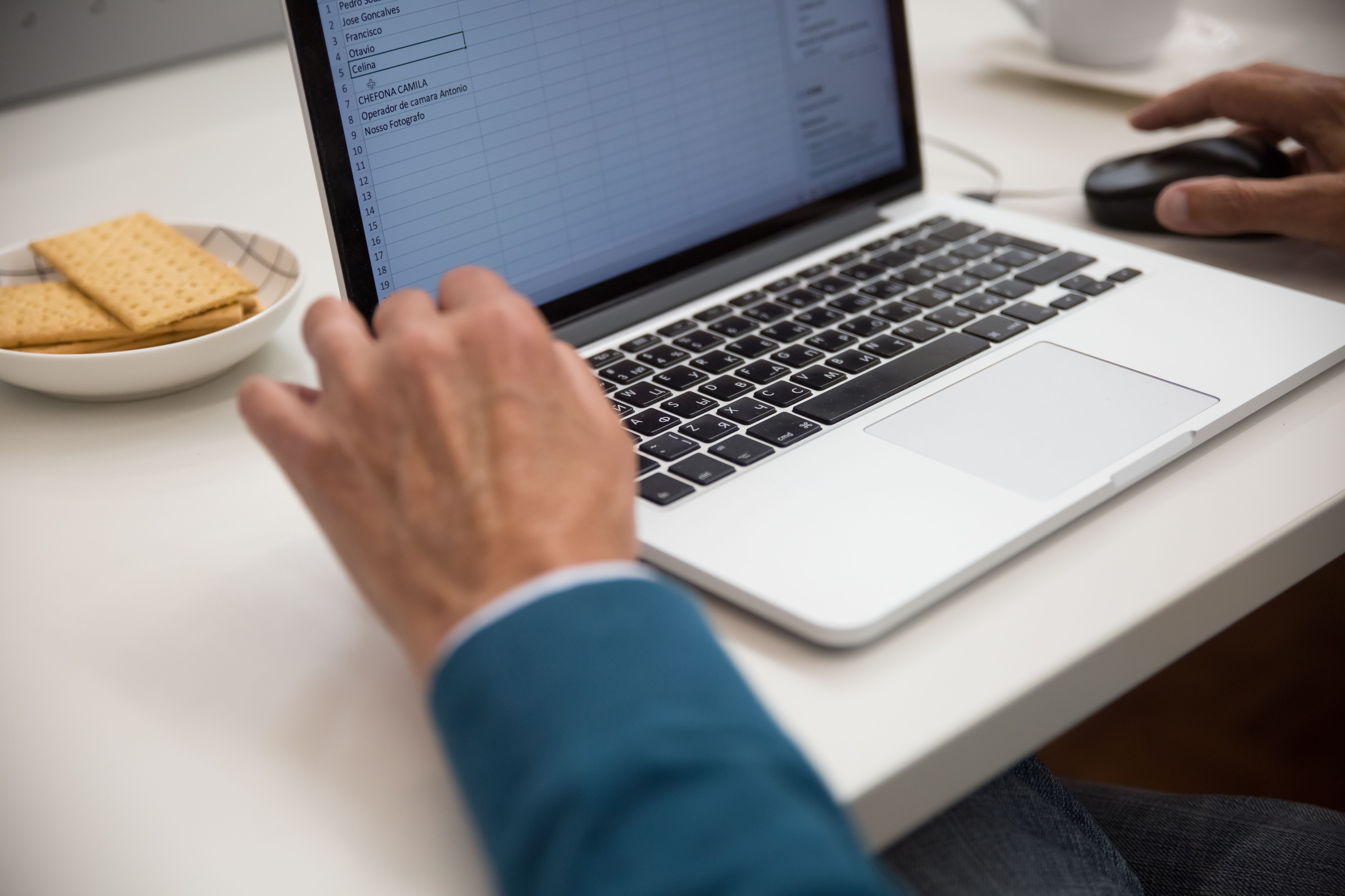 Eine Person arbeitet an einem Laptop mit geöffneter Tabelle, daneben ein Teller mit Keksen
