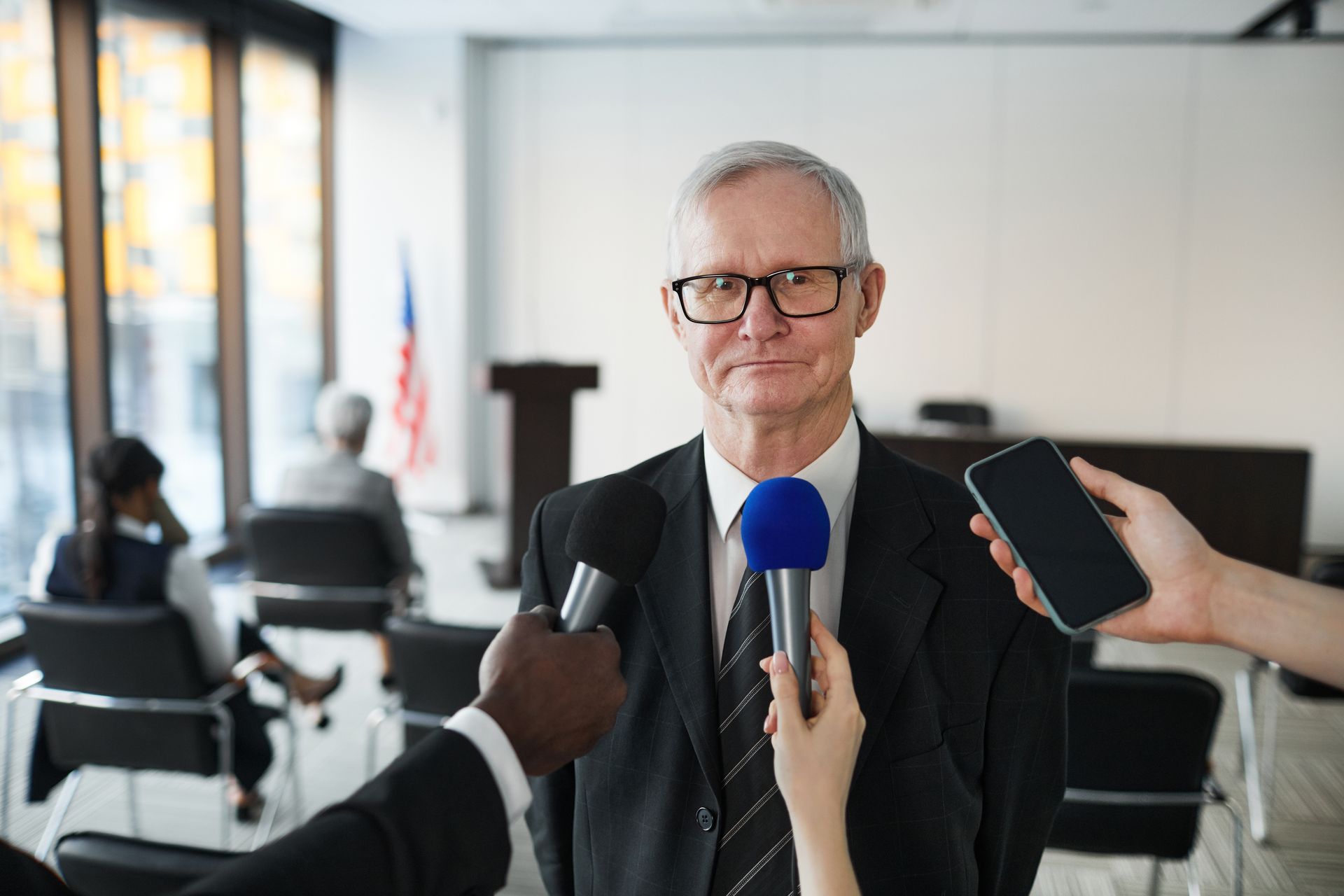 Mann im Anzug beantwortet Fragen von Journalisten mit Mikrofonen