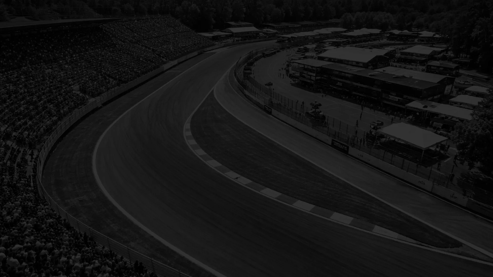 Circuit de course en virage avec gradins remplis de spectateurs à gauche et bâtiments à droite.