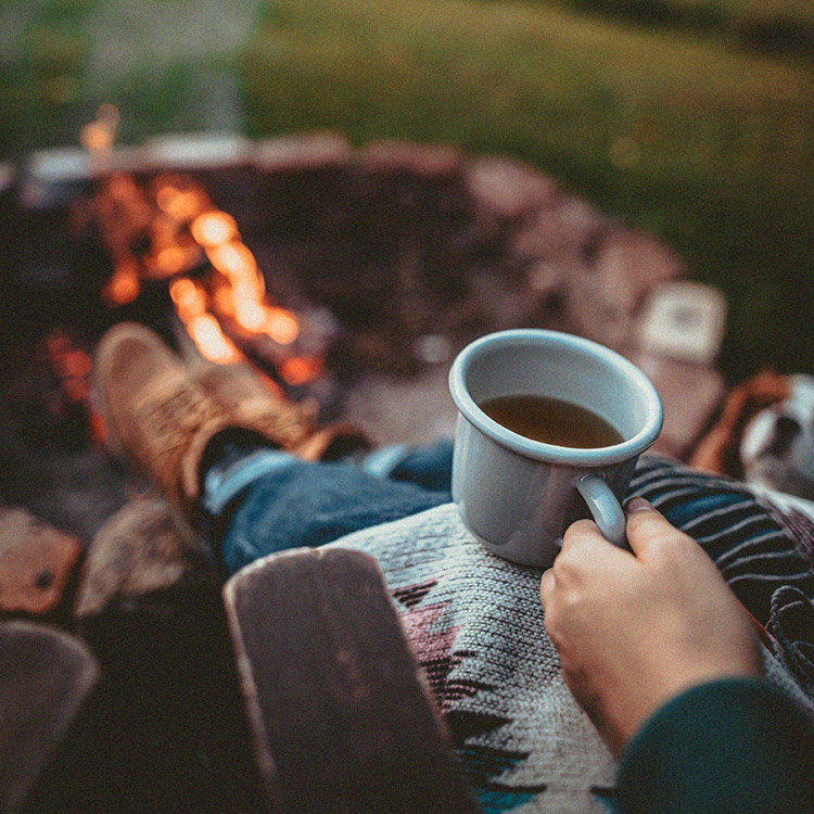 Image of a person enjoying a cup of coffee around a campfire.